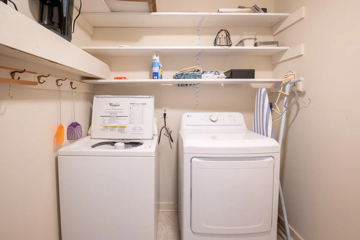 A practical laundry and storage area featuring a washing machine, drying machine, shelving, and an ironing board. This interior shot highlights utility and organization, supporting gear prep and post-adventure cleanup.