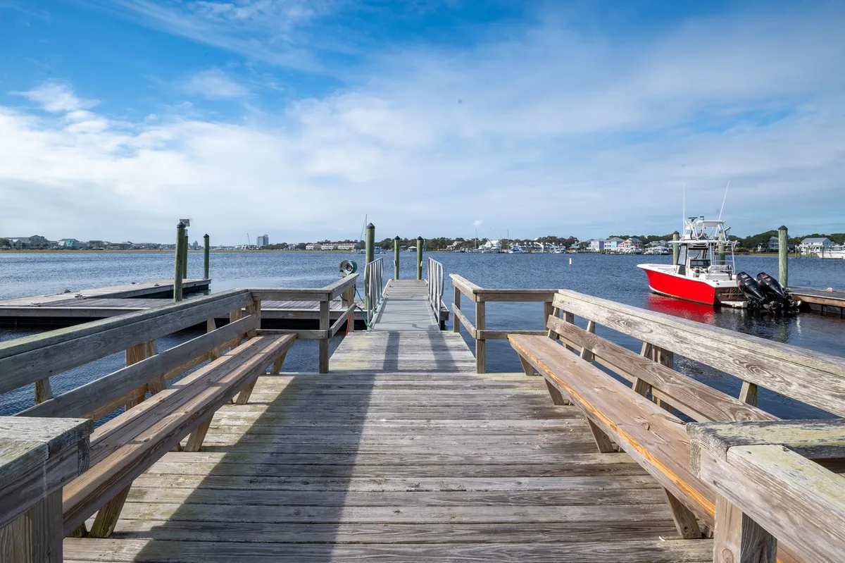 A tranquil exterior scene featuring a wooden dock leading out over calm water, with a red boat docked alongside. The sky is peaceful and the setting appears ideal for boating, fishing, or simply relaxing by the water.