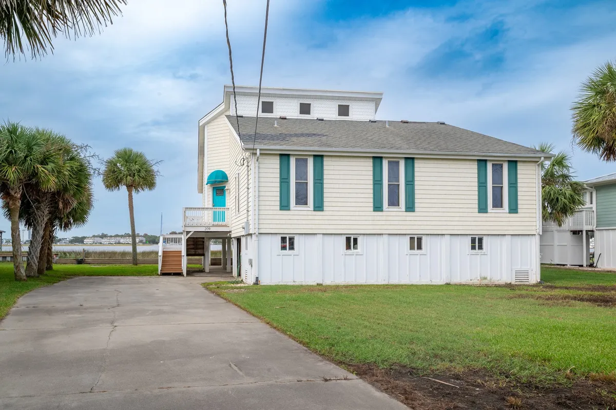 An exterior shot showcasing the front porch surrounded by palm trees with blue accents on the windows. The setting is relaxed, suggesting easy outdoor living and proximity to the waterfront.