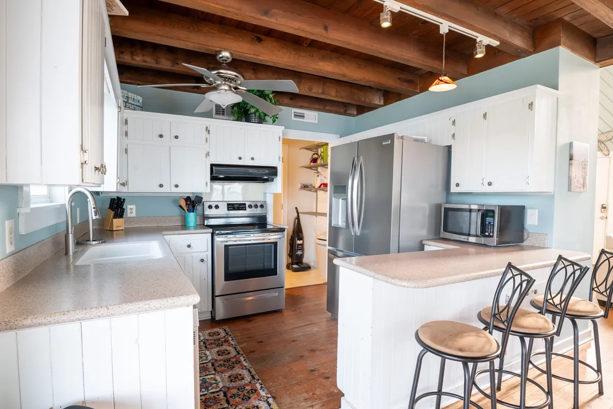 A modern kitchen featuring a central island, stainless steel appliances, wooden beams, and ample workspace. The space is designed for family gatherings, cooking, and easy meal prep.