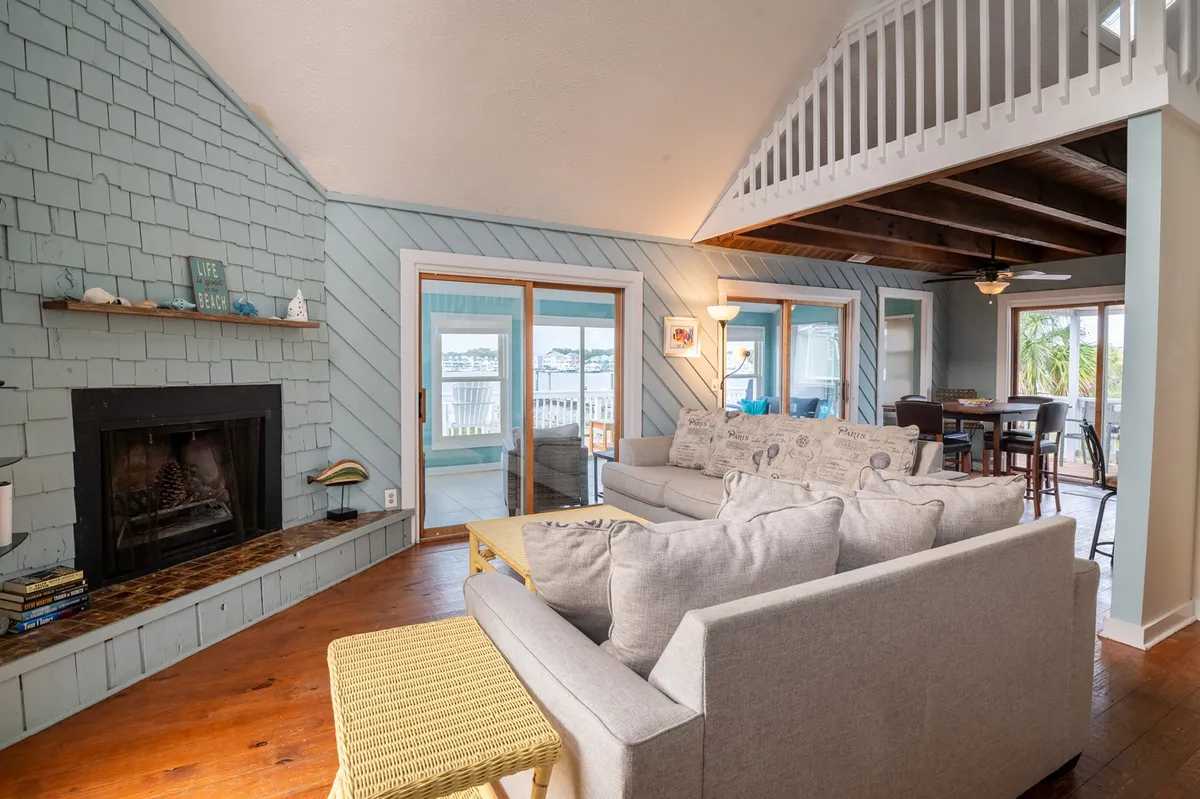 A casual living room with a fireplace, comfortable seating, decorative accents, and large windows letting in plenty of daylight. The space feels perfect for relaxing after a day at the beach or planning your next local adventure.