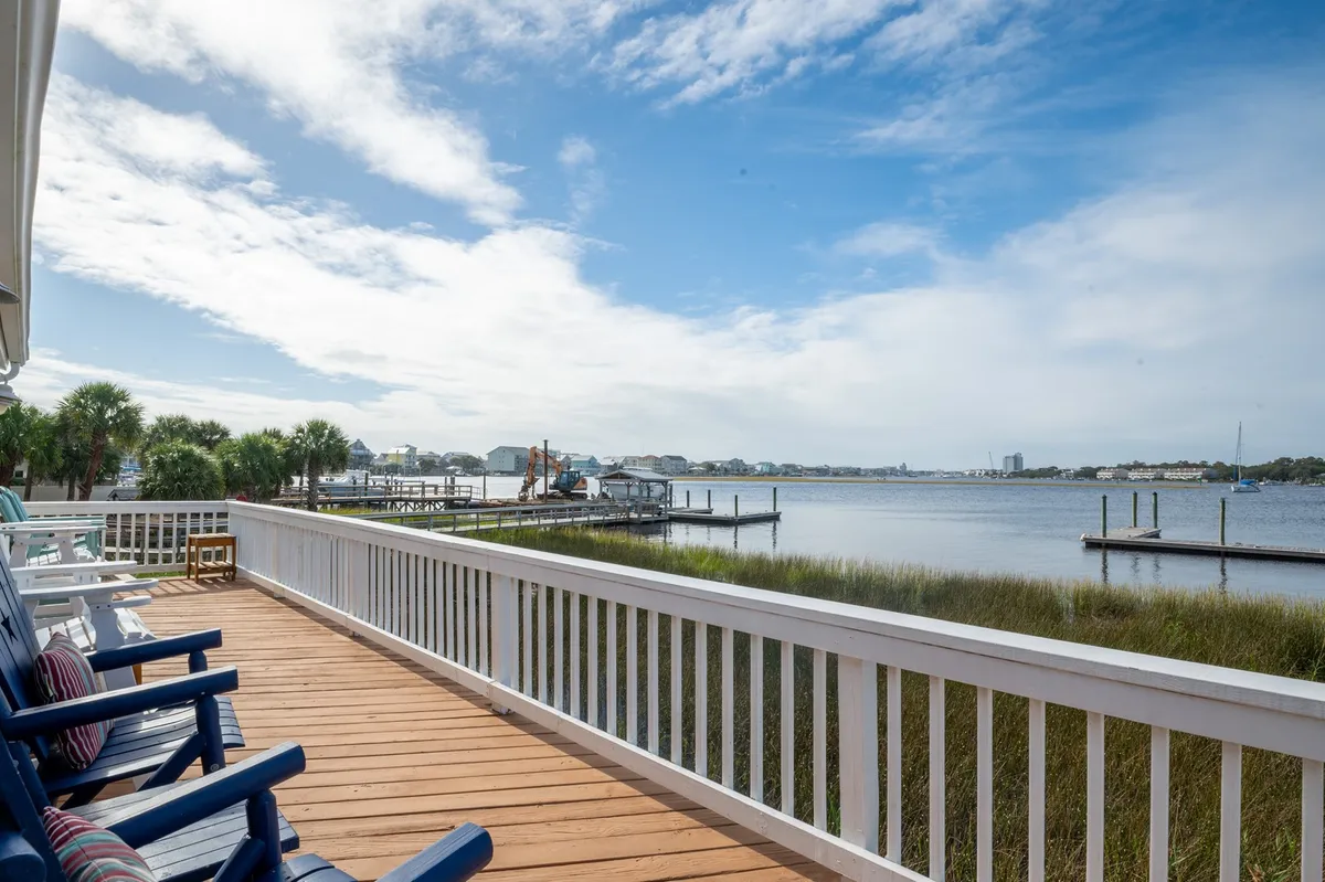 A serene waterfront view with a wooden deck, lounge chairs, and a distant marina. The deck provides direct access to the water and is perfect for relaxing, launching boats, or gearing up for a fishing trip.